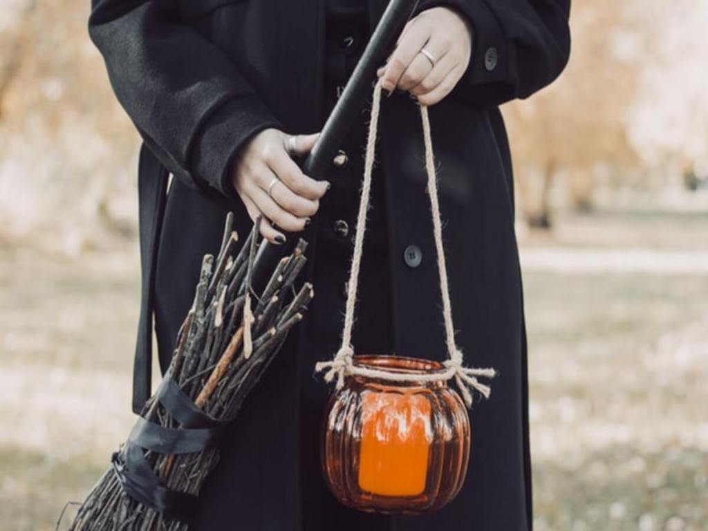 A witch holding a broom and a small cauldron.