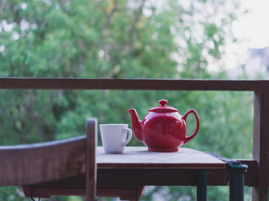 A red teapot with a white cup on a wooden table.