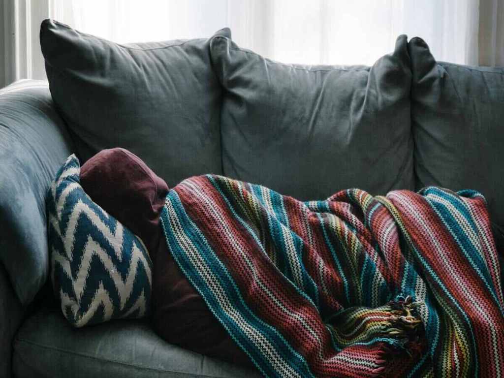 A person sleeping on a sofa and covered with a blanket.