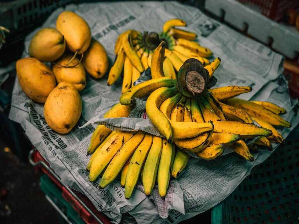 Bananas and papayas on a table with old newspapers.
