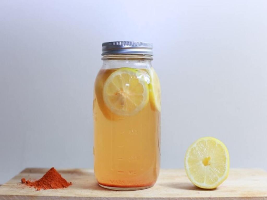 A glass jar with sliced lemons and red spices on a table.