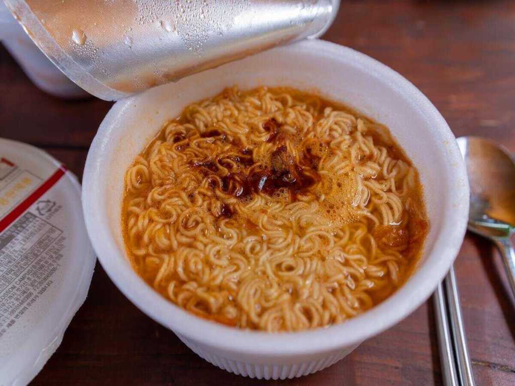 An opened cup of instant noodles with seasoning.