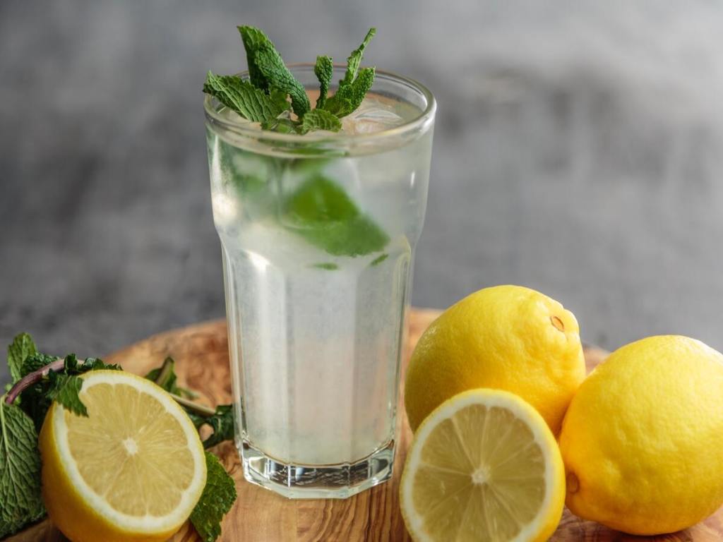 A glass of fresh lemon water with lemons on a table.