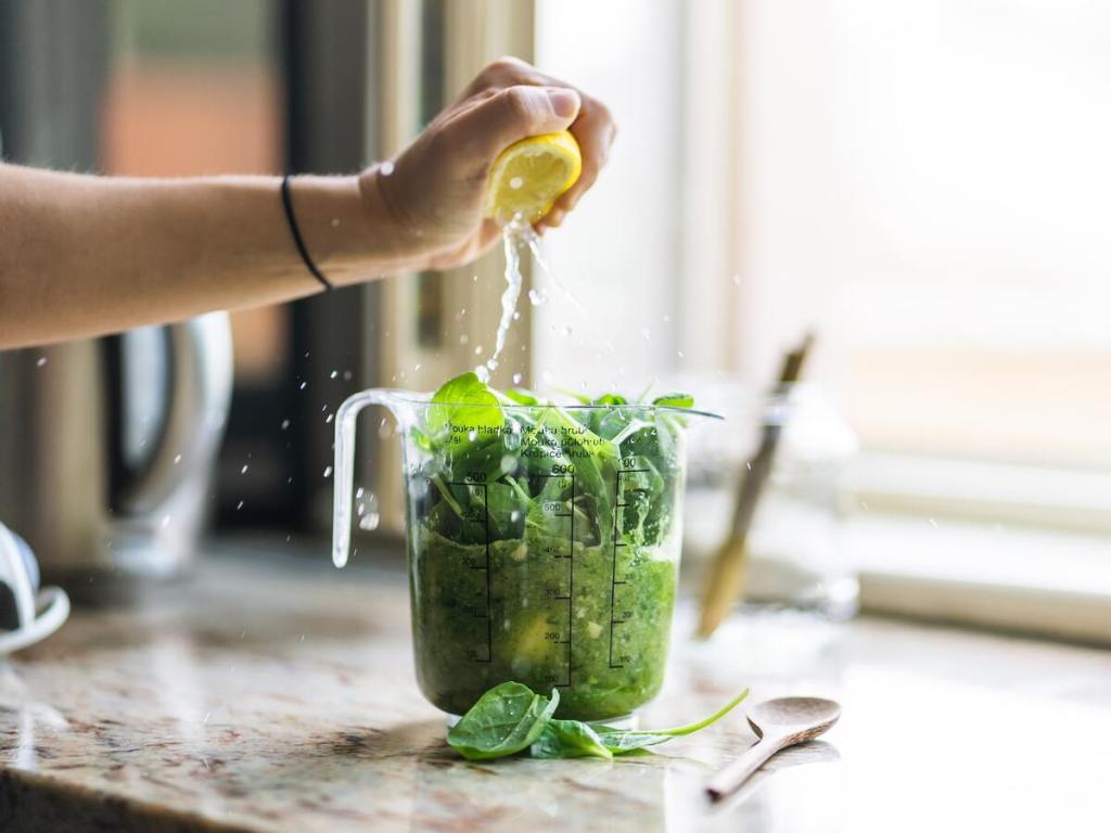 A jar filled with kale and squeezing a lemon on top.