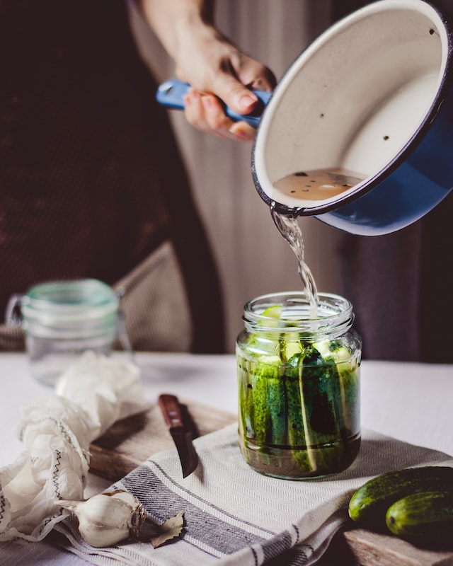 Adding brine to the jar of sliced cucumbers.