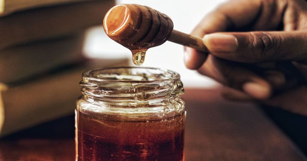 A jar of honey with a hand holding a wooden honey spoon.