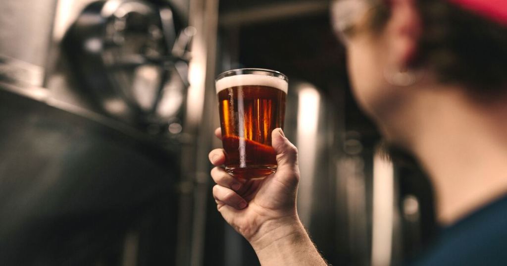 A brewer checking the clarity of a glass of beer.