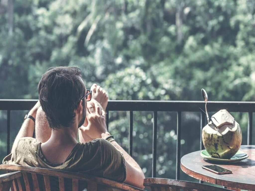 A man relaxing on a balcony with a fresh coconut drink.
