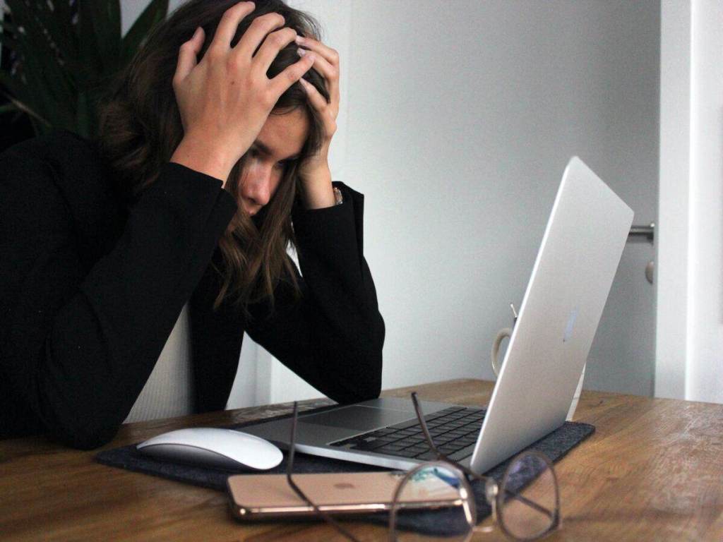 A woman holding her head in front of a computer.
