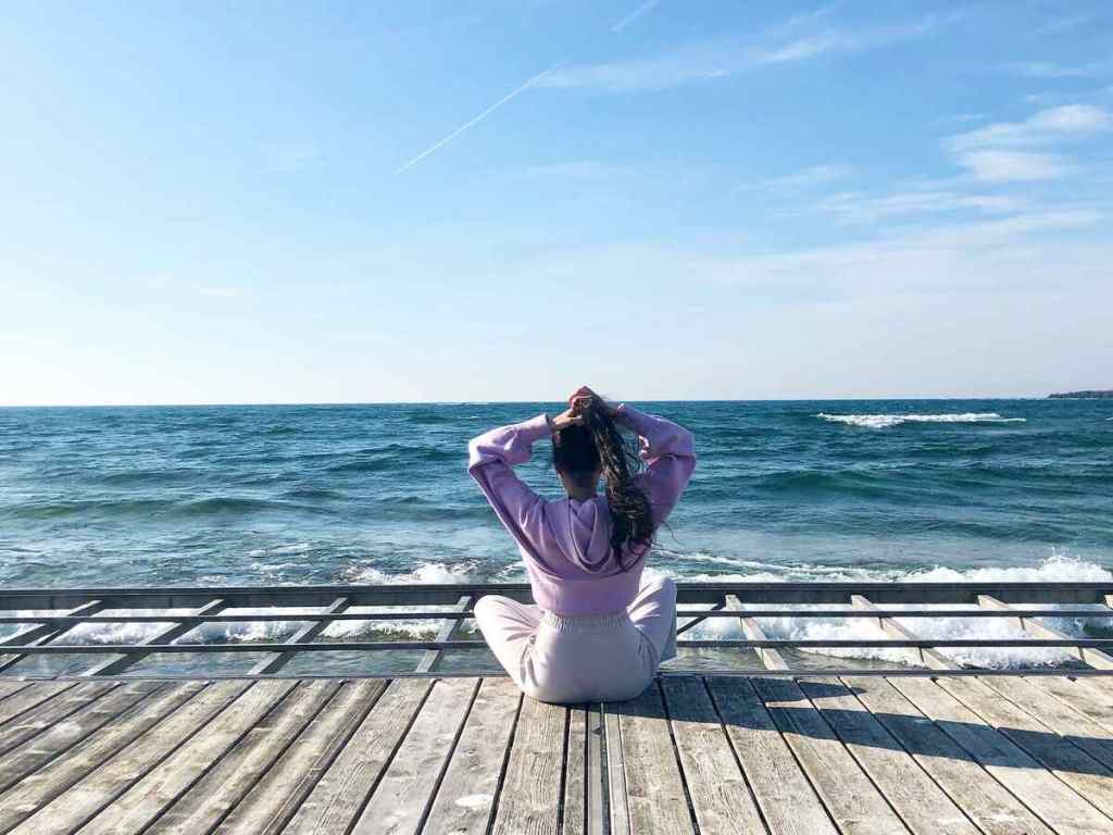 A woman sitting on the edge of the seashore with the wind in her hair.