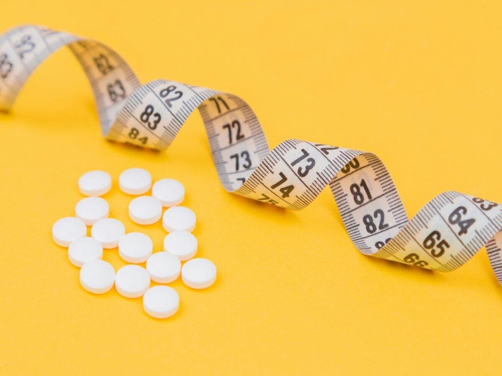 White pills next to a measuring tape.