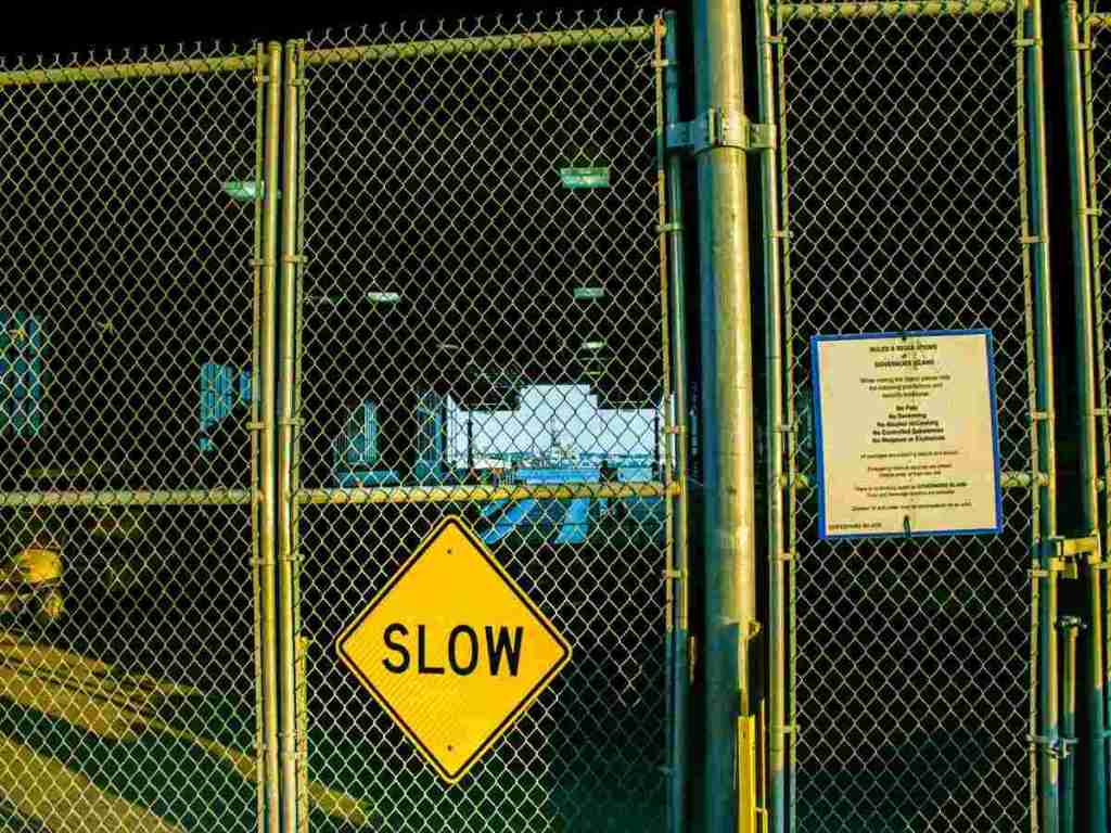 A yellow slow sign was posted on a metal fence.