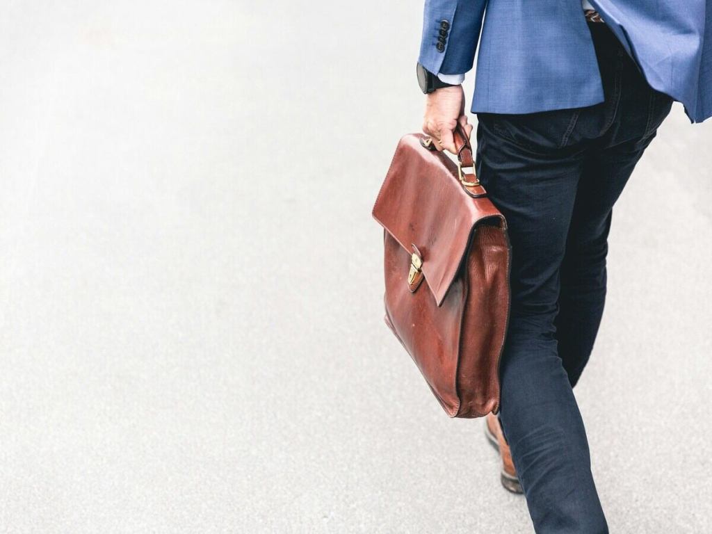 A man walking and holding a leather briefcase.