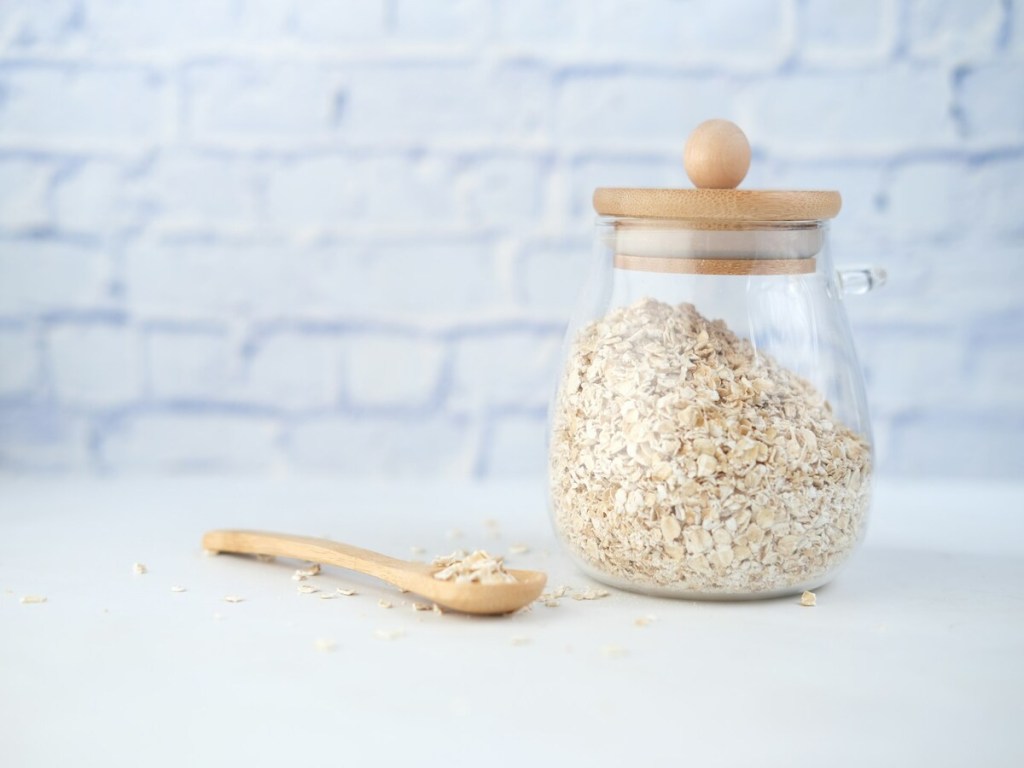 A glass container with oats and a wooden spoon.