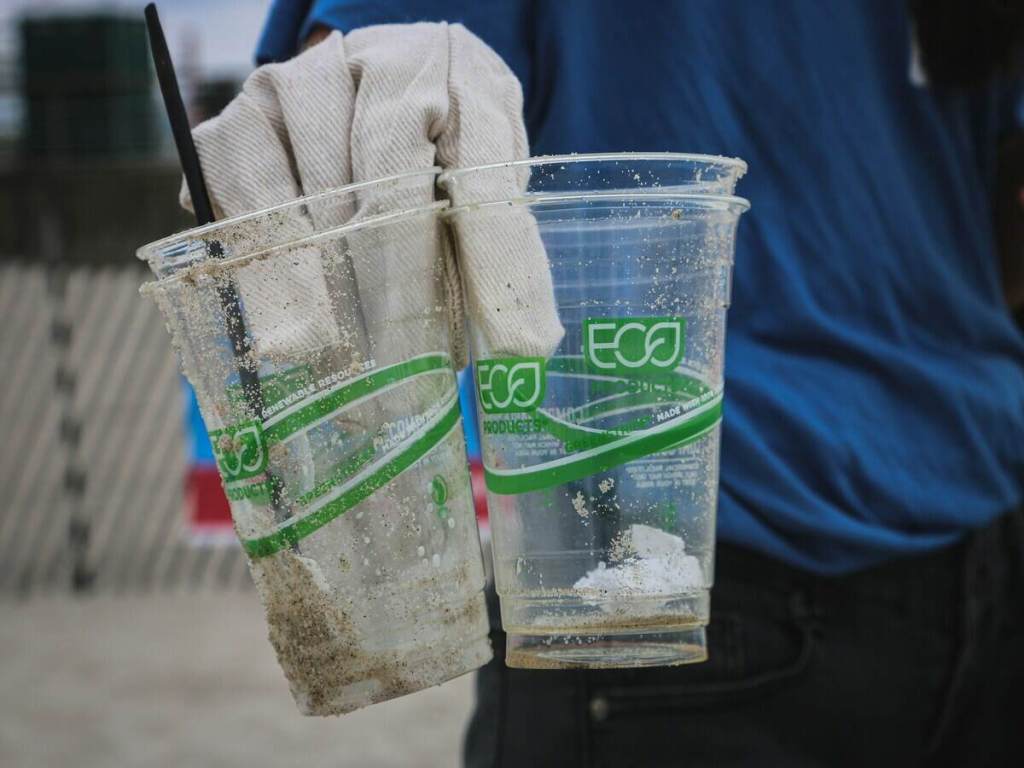 A person holding 2 plastic cups with eco written on them.