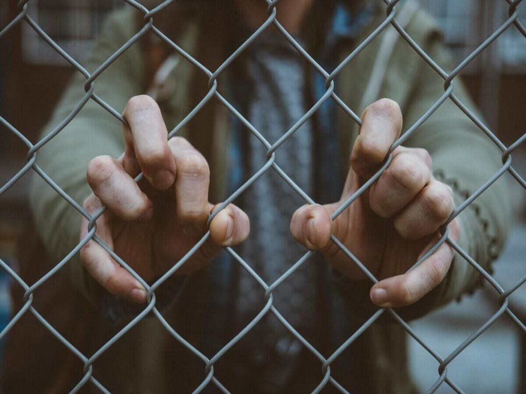 Someone touching a metal fence with his fingers.