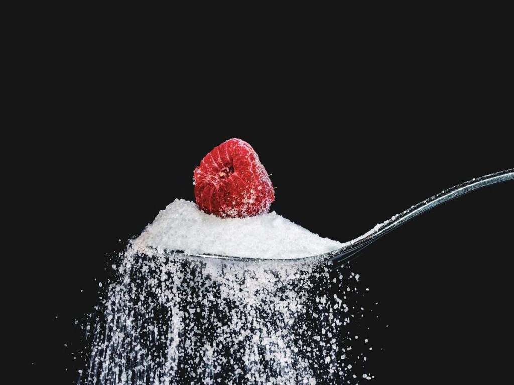 A spoon of powdered sugar with a raspberry on top.