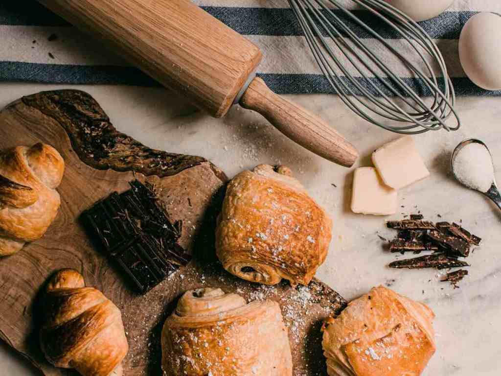 Baked pastry with butter, sugar, and wooden roller ready on a table.