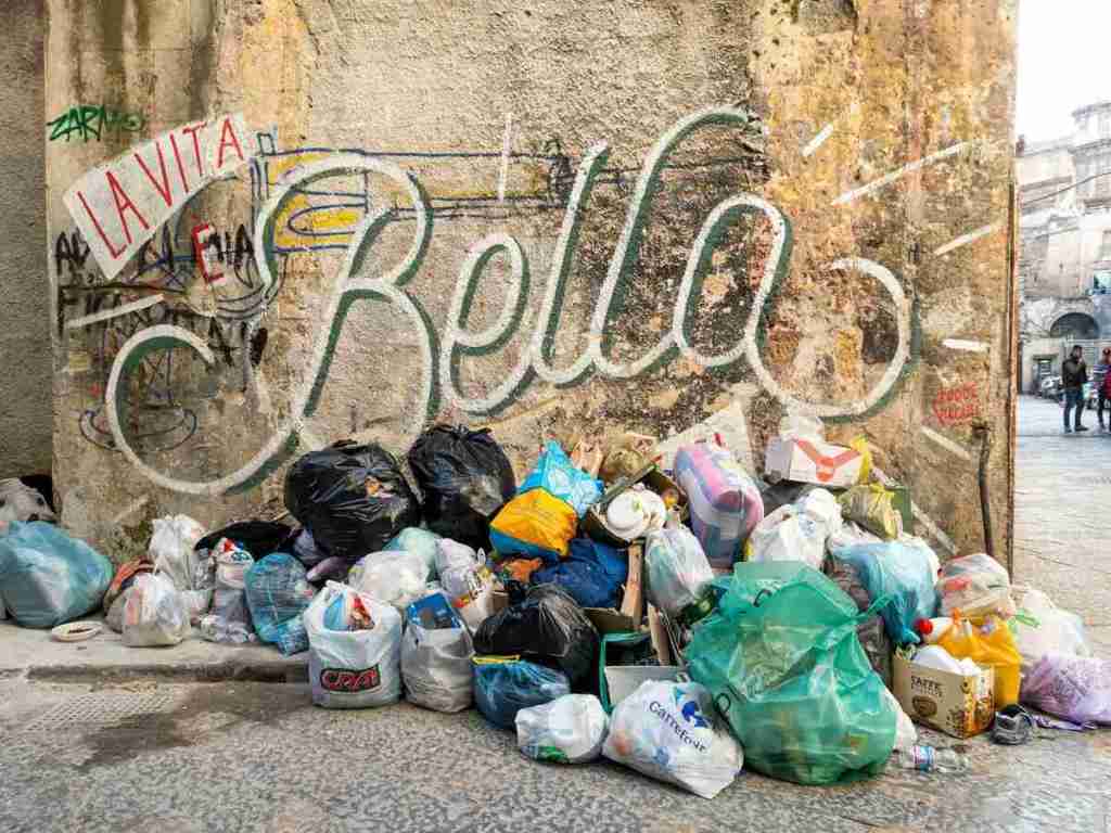 The trash in plastic bags collected next to a wall with graffiti.