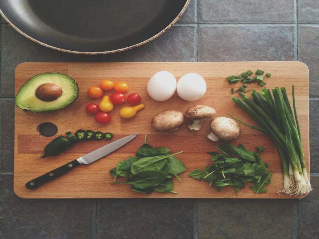 A cutting board with a knife, eggs, avocado, mushrooms and leeks.