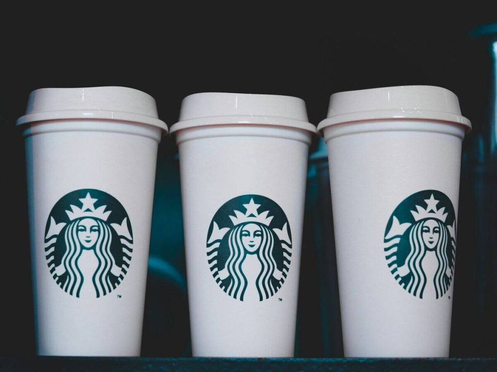 Three white Starbucks coffee cups on a black background.