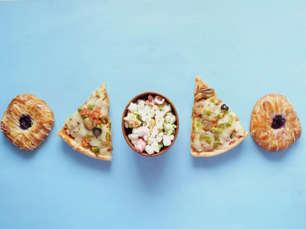 A row of pastries, pizza slices and popcorn on a blue background.